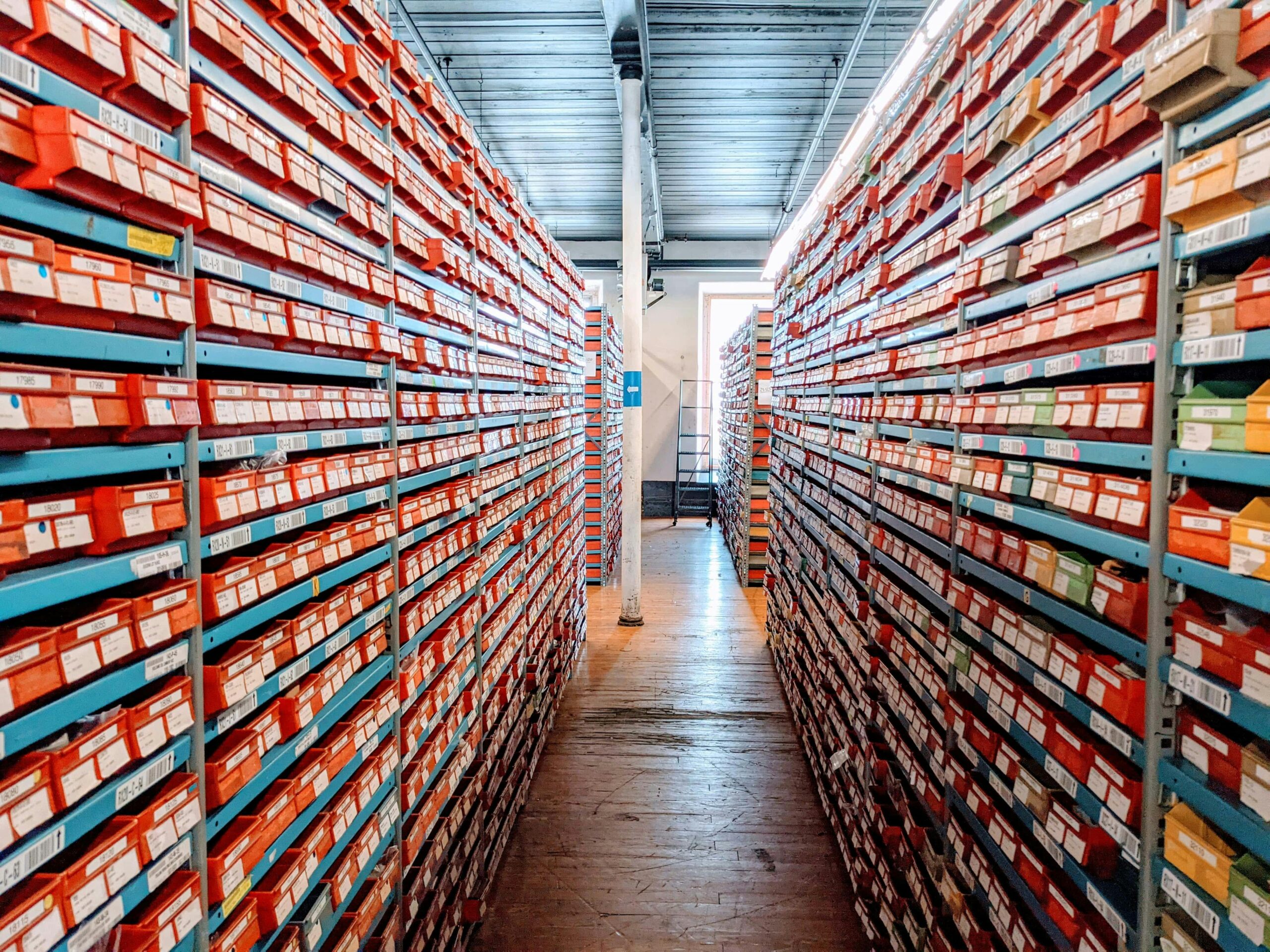 A well-organized warehouse aisle filled with red shoe boxes on shelves, showcasing efficient inventory storage.